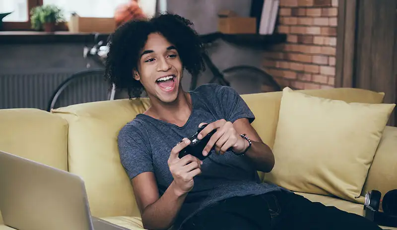 Ready to Play: No Driver Needed. A teenager is playing console game on a couch and using LGHD2 to capture his gameplay.